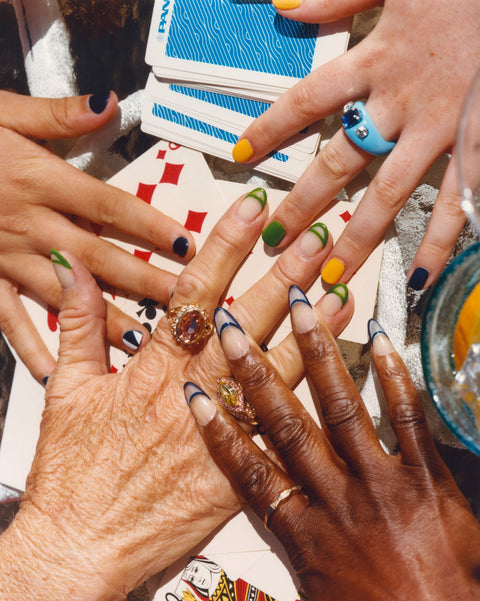 Close up of multiple hands with painted nails resting on top of a deck of playing cards.